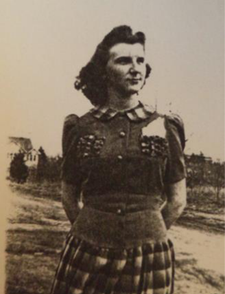 A black and white image of Margaret Duke. She had shoulder-length hair that is being blown in the wind. She wears a plaid skirt that matches the collar of her shirt. There are two pockets on her chest with something in the right one. There are buttons down the front of her shirt. In the back left corner a house can be seen.